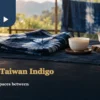 Indigo-dyed cloth on a wooden table beside white porcelain tea ware, with another blue textile hanging behind