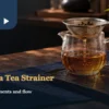 A tea strainer above a glass pitcher beside a tea cup